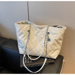 Detailed close-up of ivory quilted tote bag with silver chain straps and metallic pendant