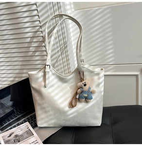 Detail of white leather tote bag with a cute teddy bear charm and fashion logo print