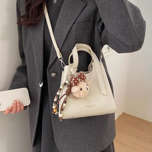 Detail of beige bucket bag with leather texture, plush bear charm and metallic feet