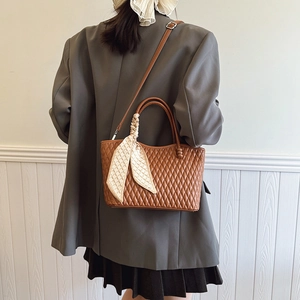 Detalle de bolso acolchado marrón oscuro con elegante pañuelo de cuadros en el asa