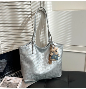 Detailed shot of silver metallic tote bag with bear charm and brand text on front