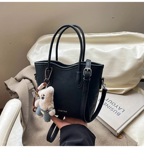 Détail du sac seau en cuir noir avec logo doré et breloque ours en peluche