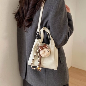 Detail of cream bucket bag with lychee texture featuring a teddy bear charm and beads