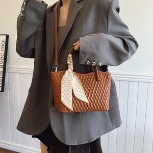 Detalle de bolso acolchado marrón con asa de seda sobre un conjunto de blazer gris