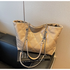 Detail of beige quilted tote bag featuring glossy finish and silver chain shoulder strap