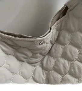 Detail of beige quilted tote bag showing soft fabric texture and silver rivet closure