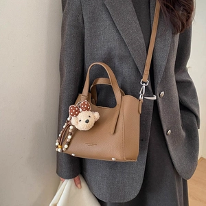 Brown bucket bag with litchi texture leather and cute bear charm shown on model