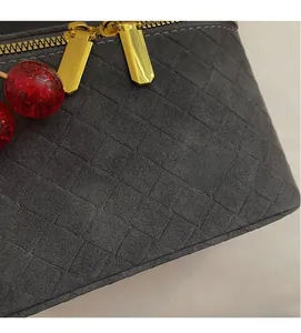 Detail of dark gray suede woven bag featuring dual gold zippers and a red cherry charm