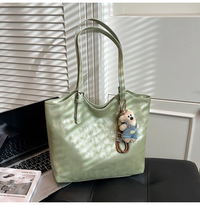 Close-up of a light green metallic tote bag with bear charm and fashion text detail