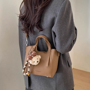 Brown lychee leather bucket bag detail featuring a cute plush bear pendant accessory