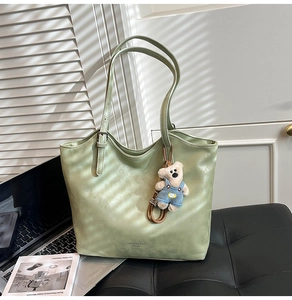 Detail of light green leather tote bag with fashion slogan and bear charm accessory