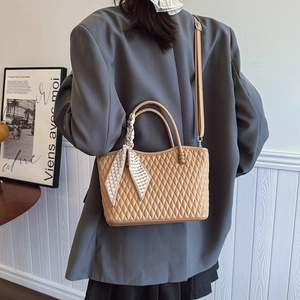 Detalle de bolso acolchado caqui con asa de seda estampada y correa fina para hombro