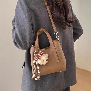 Detail of dark brown pebble leather bucket bag with teddy bear charm and logo print