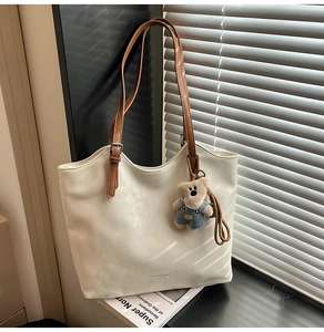 Detail of cream tote bag featuring brown leather handle and cute teddy bear charm