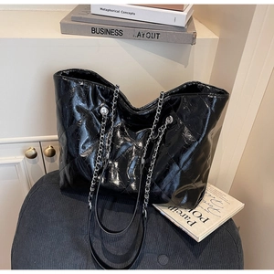 Detail of quilted glossy leather texture and silver chain strap on a large black tote bag