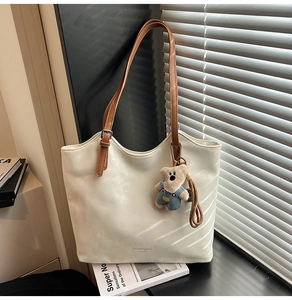 Detail of white leather tote bag with brown straps and cute teddy bear charm accessory