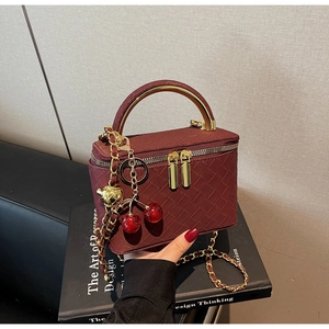 Detailed view of dark red woven texture box bag with gold metal handle and cherry charm