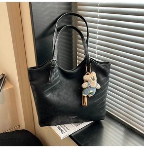 Detail of black tote bag featuring textured PU leather, adjustable buckle, and bear pendant