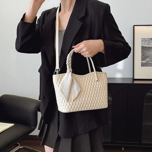 Detalle de bolso acolchado beige con asa envuelta en un pañuelo de seda a cuadros