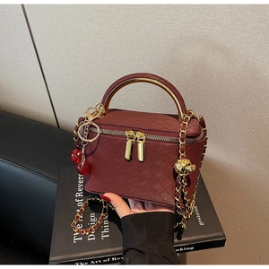 Close-up of wine red woven texture box bag with golden handle and cherry charms