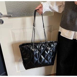 Detail of black quilted tote bag with glossy finish and chain shoulder strap