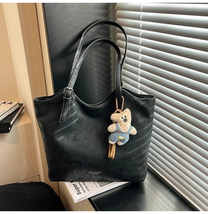 Detail of large black leather tote bag with fashion lettering and cute teddy bear charm