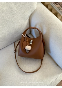 Detail of brown lychee grain bucket bag with heart tag and ice cream charm on sofa