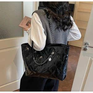 Detail of black quilted leather tote bag with metal chain strap worn by a female model