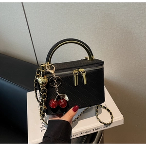 Detail of black woven vanity bag featuring golden handle, chain strap and cherry charm