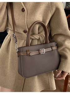 Sac à bandoulière minimaliste en cuir marron foncé avec boucle argentée sur manteau beige