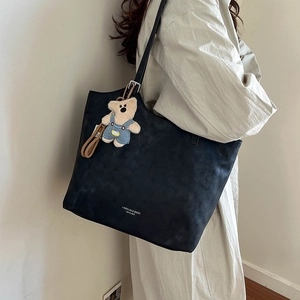Detail of black tote bag featuring leather texture, metal buckle and cute bear charm
