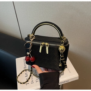 Detail of black woven texture vanity bag with gold handle and cherry charm accessory