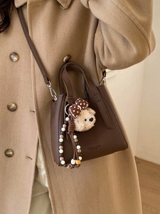 Brown lychee leather bucket bag with cute bear charm worn over a camel wool coat