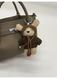 Close-up of plush bear charm in brown knit hoodie on a leather bucket handbag