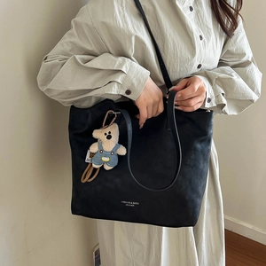 Detail of black leather tote bag with long straps and a plush bear charm on a model