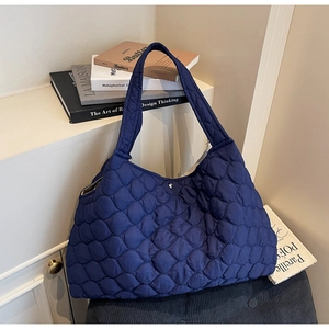 Detail of navy blue quilted puffer tote bag resting on books in a stylish setting