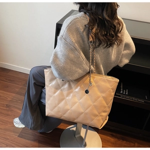 Detail of quilted leather tote bag with elegant chain strap and circular pendant charm