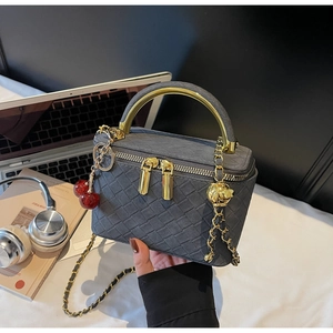 Gray woven box handbag with golden metal handle and red cherry charm in a workspace setting