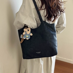 Detail of black leather tote bag with a cute bear plush charm on a model shoulder