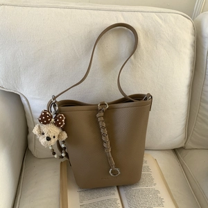 Close-up of brown litchi texture bucket bag with a cute plush dog charm on a book