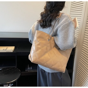 Detail of beige quilted tote bag featuring chain straps and soft faux leather texture