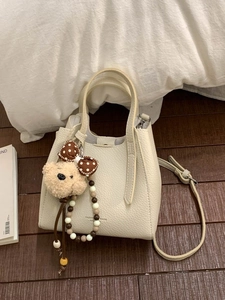 Chic beige bucket bag with plush bear charm and beaded strap on wooden floor background