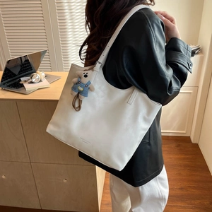 Close-up of white leather tote bag with bear charm detail and fashion text print