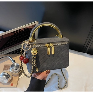 Detail of grey woven box bag featuring gold metal handle and vibrant cherry charm accessory