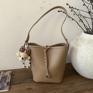 Detail of light brown bucket bag with lychee texture and plush dog pendant charm