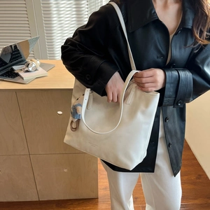White leather tote bag detail with logo text and cute bear charm shown in a lifestyle setting