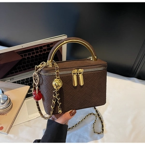 Detail of dark brown woven box bag with golden metal handle and cherry charm ornament
