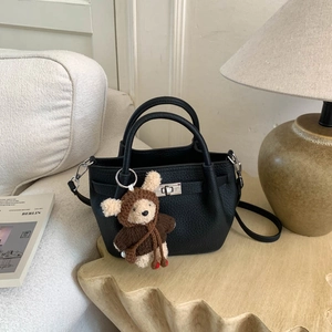 Close-up of black lychee leather bucket bag with silver turn-lock and teddy bear charm