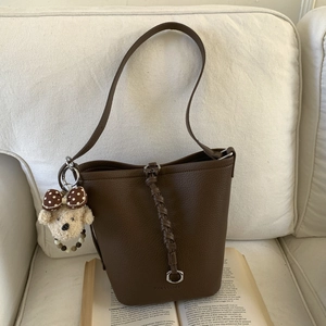 Detail of dark brown lychee leather bucket bag with woven straps and a plush bear charm