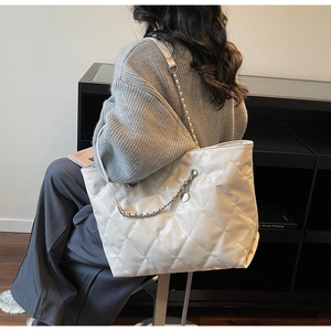 Close-up of white quilted tote bag with silver chain strap and shiny faux leather texture